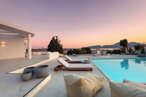 Un espace piscine extérieur moderne, doté de chaises longues et de jardinières, avec en toile de fond un magnifique coucher de soleil et des montagnes.