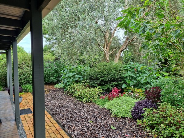 Une allée couverte, avec un chemin en briques et des parterres de jardin recouverts de paillis, où poussent différentes plantes.