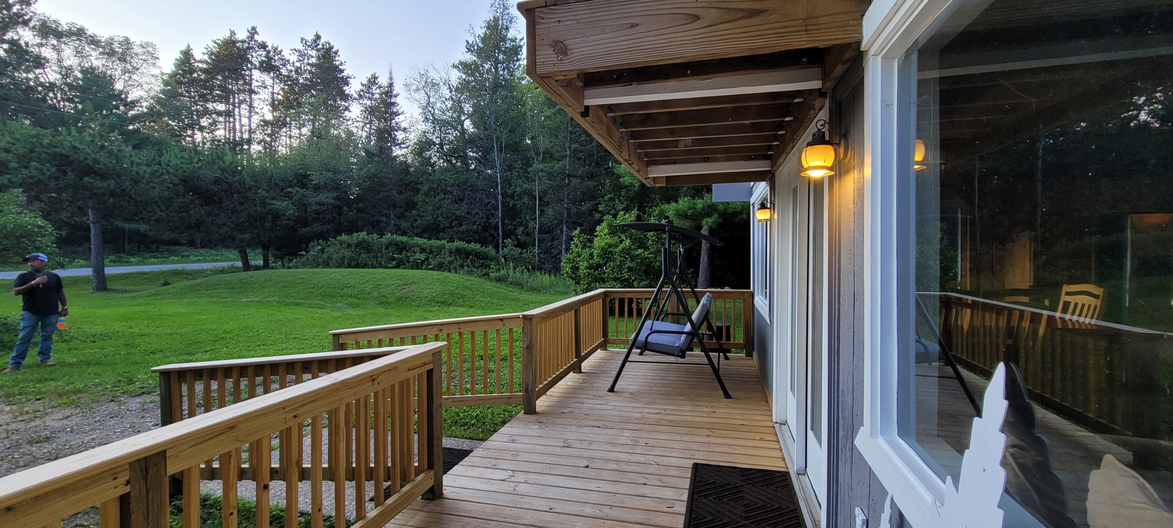 A wooden deck with a swing chair and a bench, overlooking a grassy area with trees.