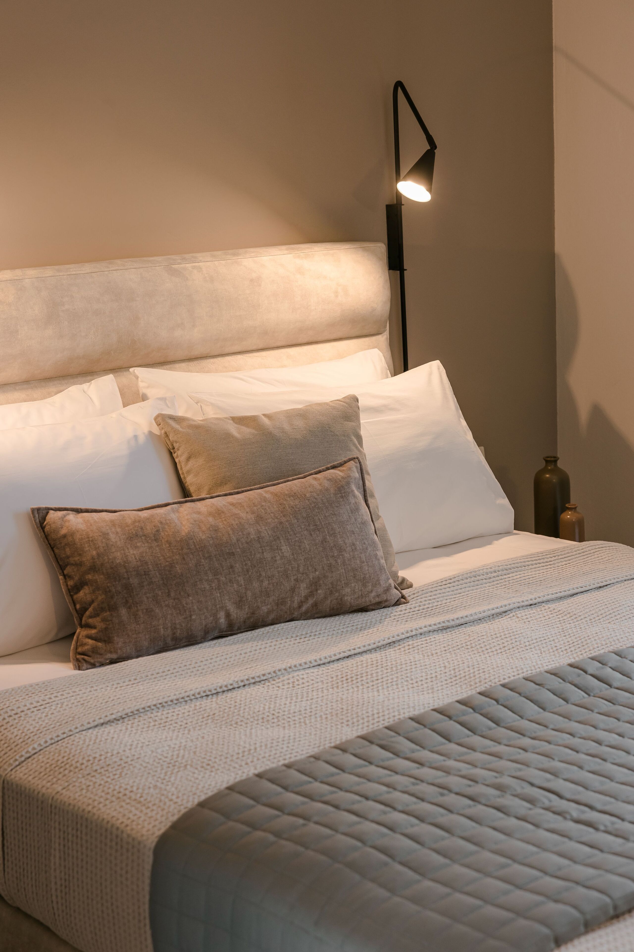 A neatly made bed with a quilted cover, two pillows, and a bedside lamp.