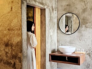 A bathroom with a large mirror, a white sink, and a wooden vanity. - Art Gate Hotel (Chiang Mai)