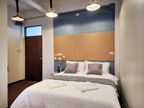 A neatly made bed with white linens and a folded towel, a wooden slatted headboard, a vase with white flowers, and two pendant lights. - Art Gate Hotel (Chiang Mai)