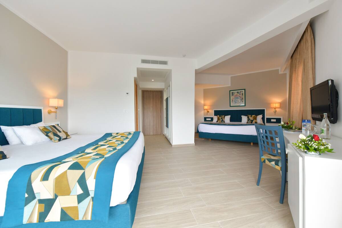 A hotel room with two beds, a desk with a TV, and a bathroom visible through an open door.