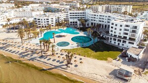 Vista aérea de un hotel con múltiples piscinas, una zona de playa con sombrillas y ubicación costera.