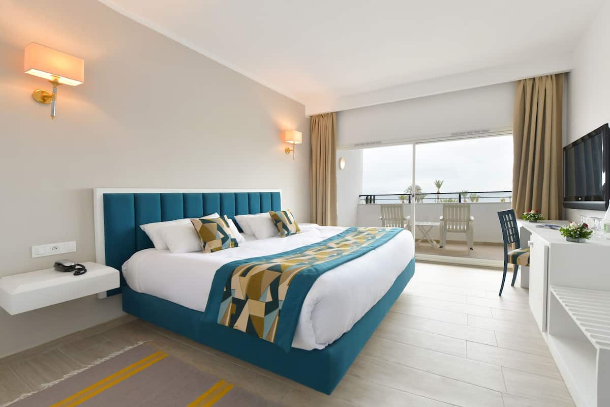 A modern hotel room with a large bed, bedside tables, a desk, and a TV.
