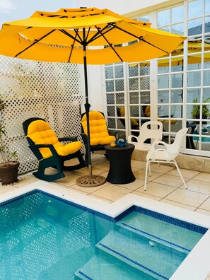 A poolside area with a yellow umbrella, two yellow cushioned chairs, a white chair, and a small round table. - The Skye High Escape- 5 mins from airport & beaches (Bon Accord)