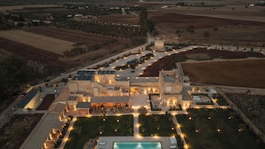 Vista aérea de un hotel con aspecto de castillo, piscina, mobiliario exterior y caminos bien iluminados.
