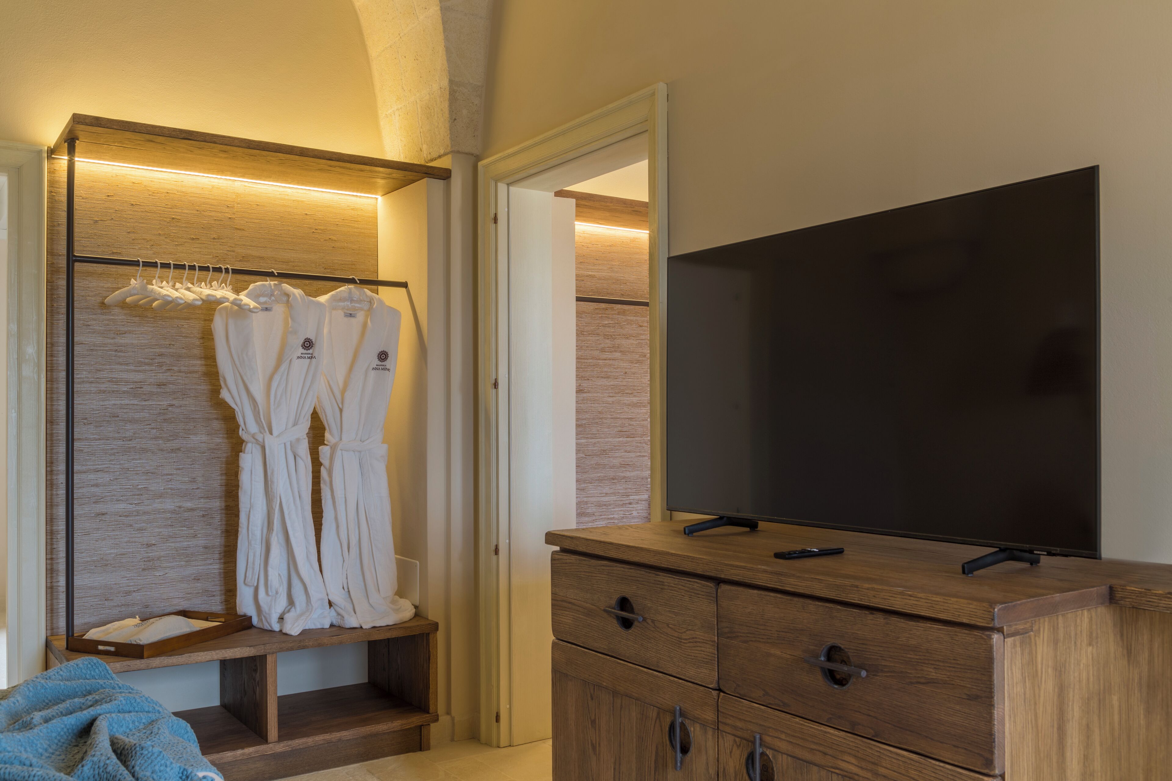 Camera d'albergo con una toeletta in legno, una TV a schermo piatto, un appendiabiti e un armadietto in legno.