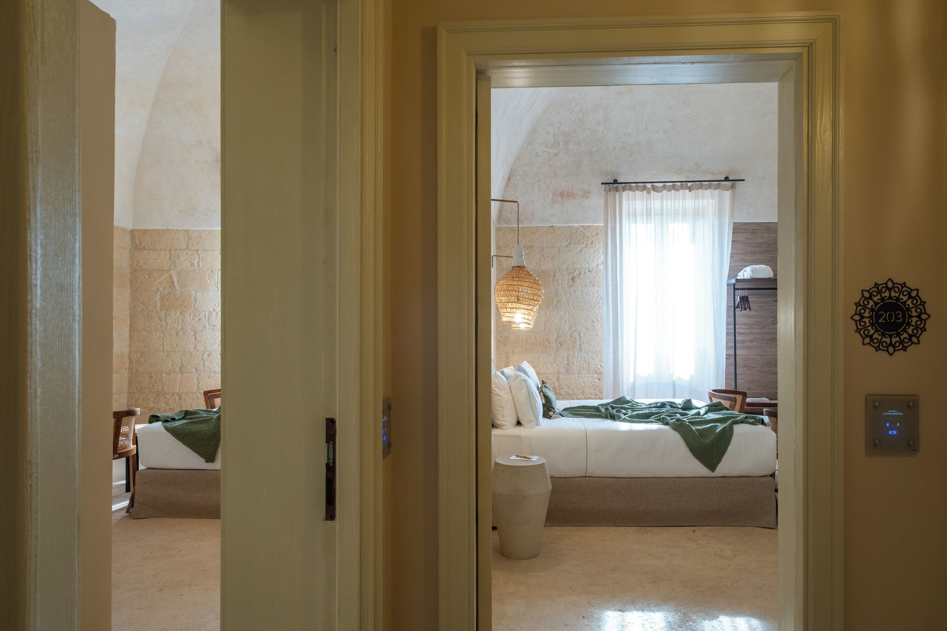 A hotel room with a bed, a bedside table, a chair, a lamp, and a wall clock.