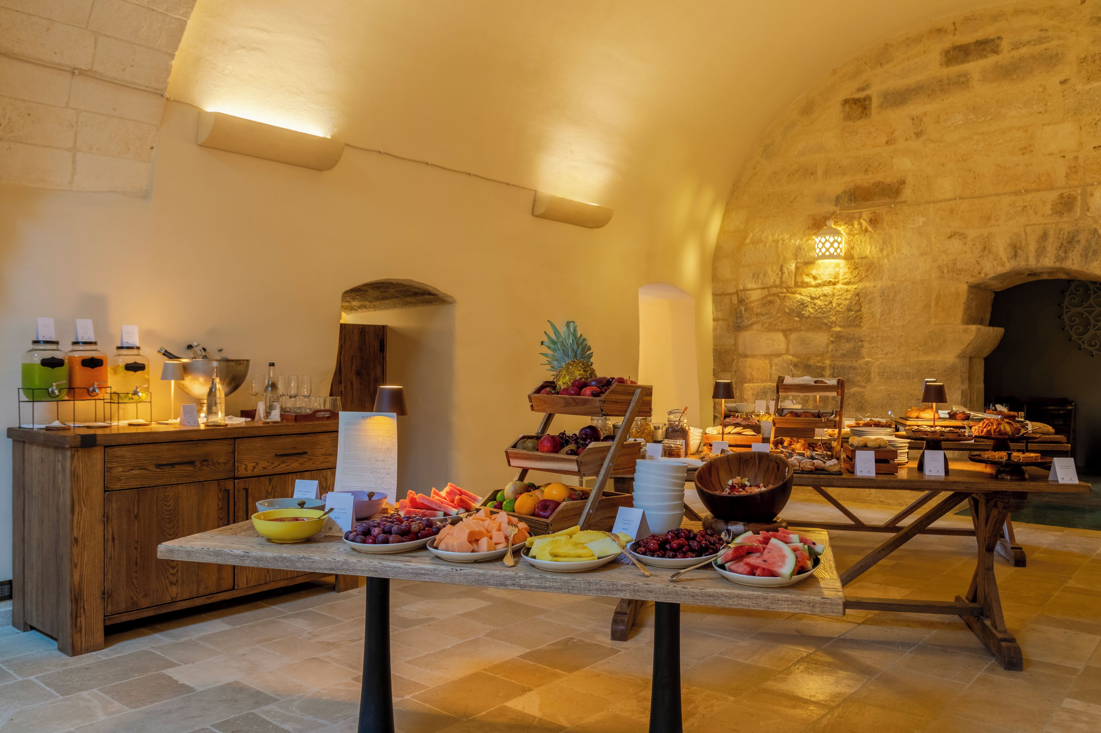 Un'area buffet con diversi cibi e bevande, un tavolo in legno e un muro in pietra sullo sfondo.