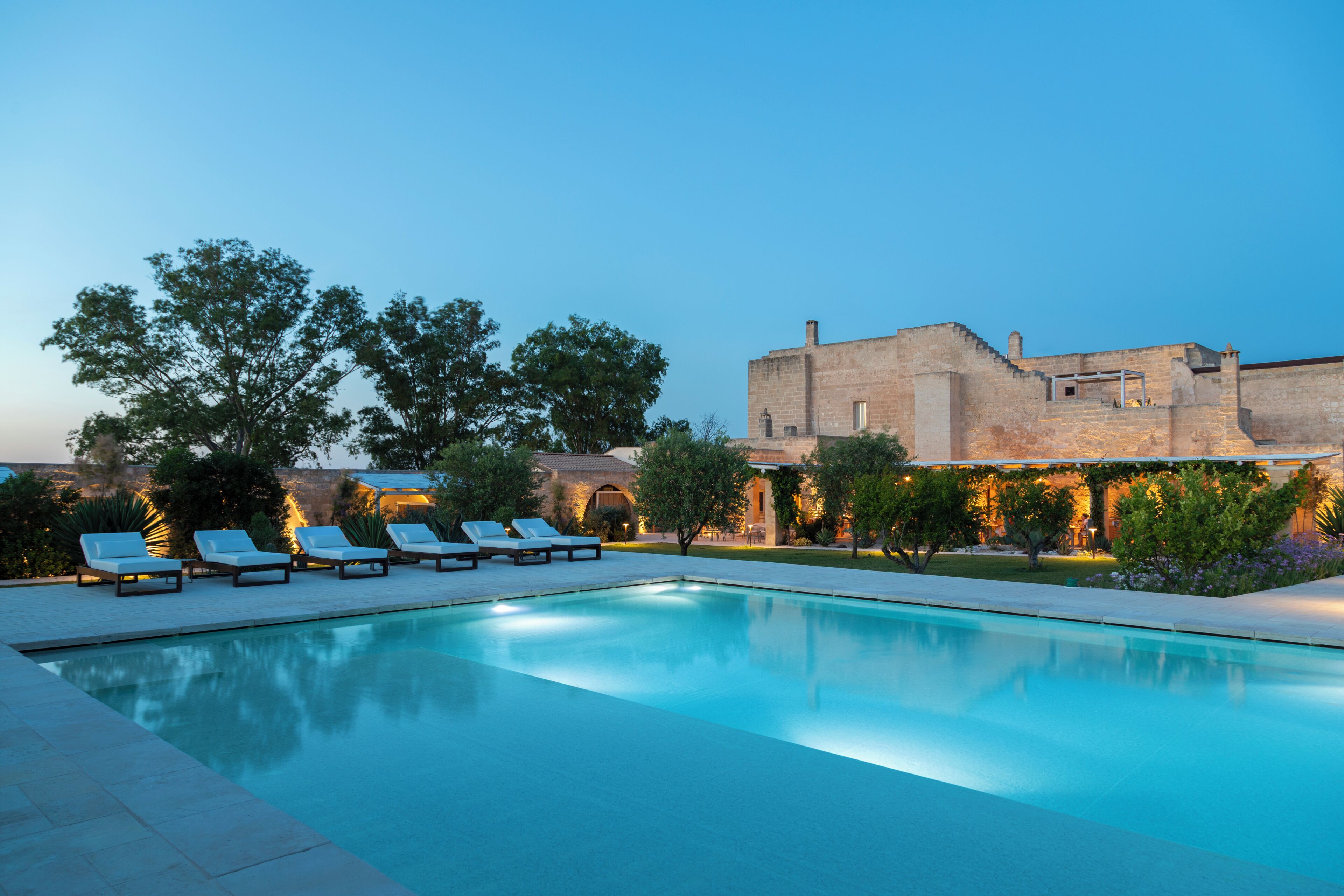 A swimming pool with lounge chairs and a stone building in the background.