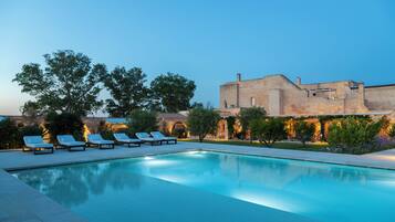 A swimming pool with lounge chairs and a stone building in the background.