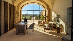 Una habitación amplia con un gran ventanal de arco, un escritorio de madera, asientos cómodos y una planta en maceta.