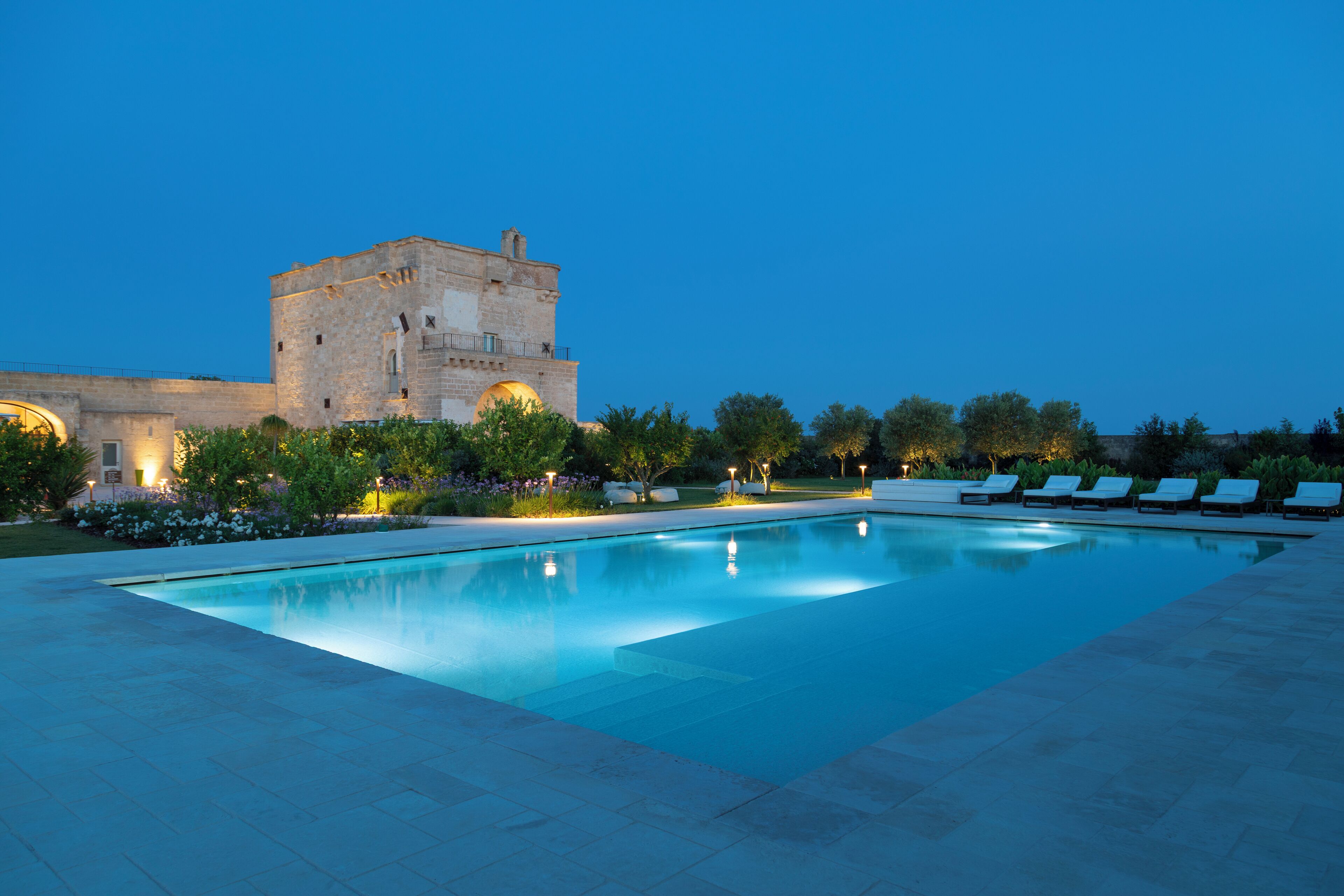 A swimming pool with lounge chairs, a stone building, and well-maintained landscaping.