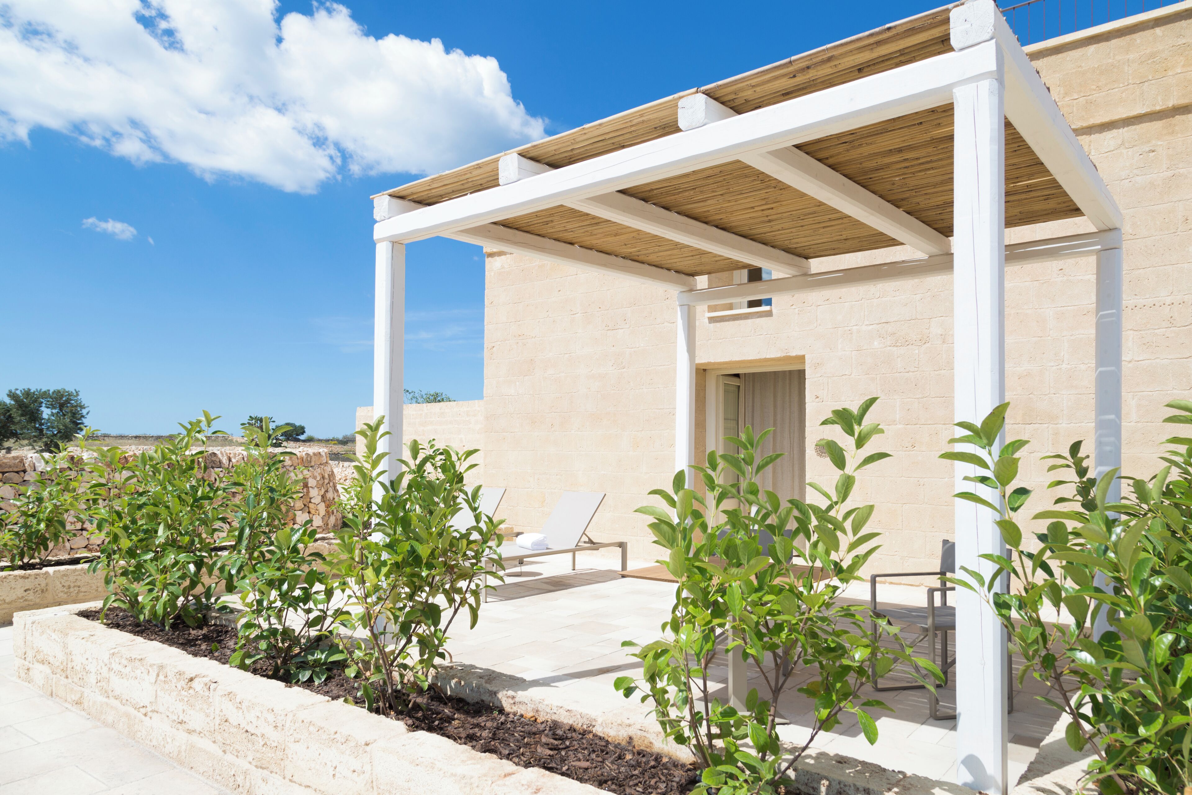 A modern outdoor patio with a pergola, seating area, and small plants.