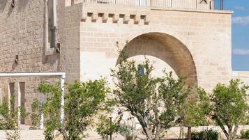 Un bâtiment historique en pierre, doté d’une grande porte en arc de cercle, d’un balcon avec une balustrade et d’une piscine en premier plan.