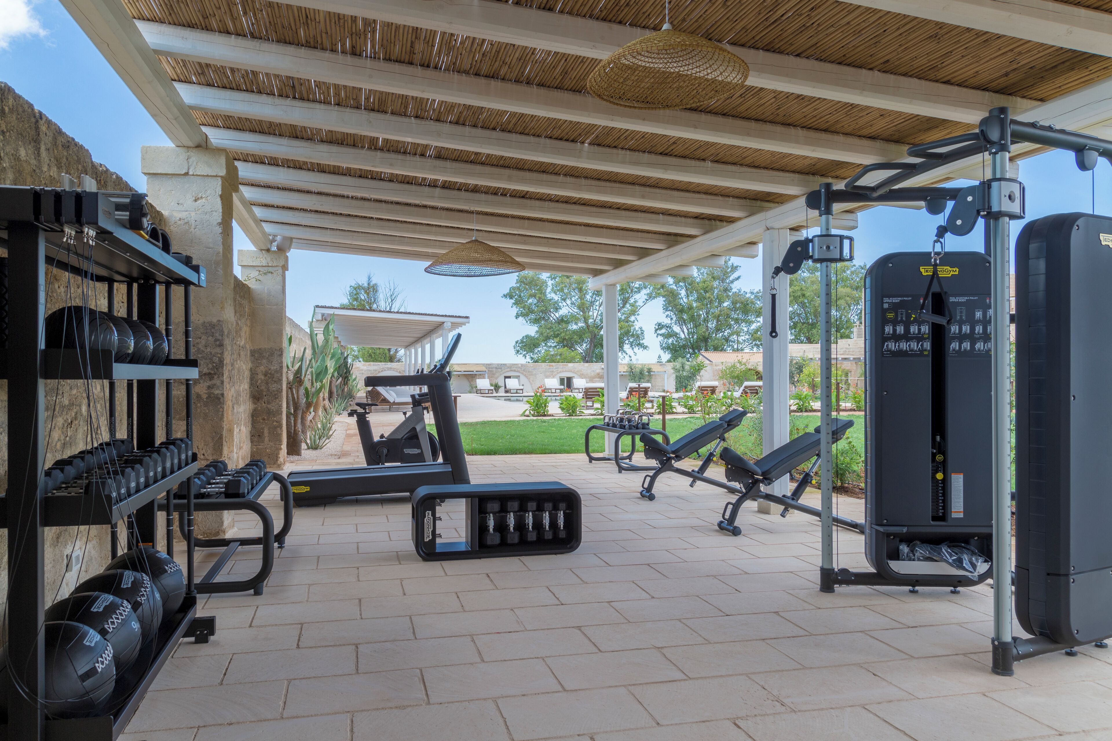 An outdoor gym area with exercise equipment, including treadmills and weight machines, under a covered roof.