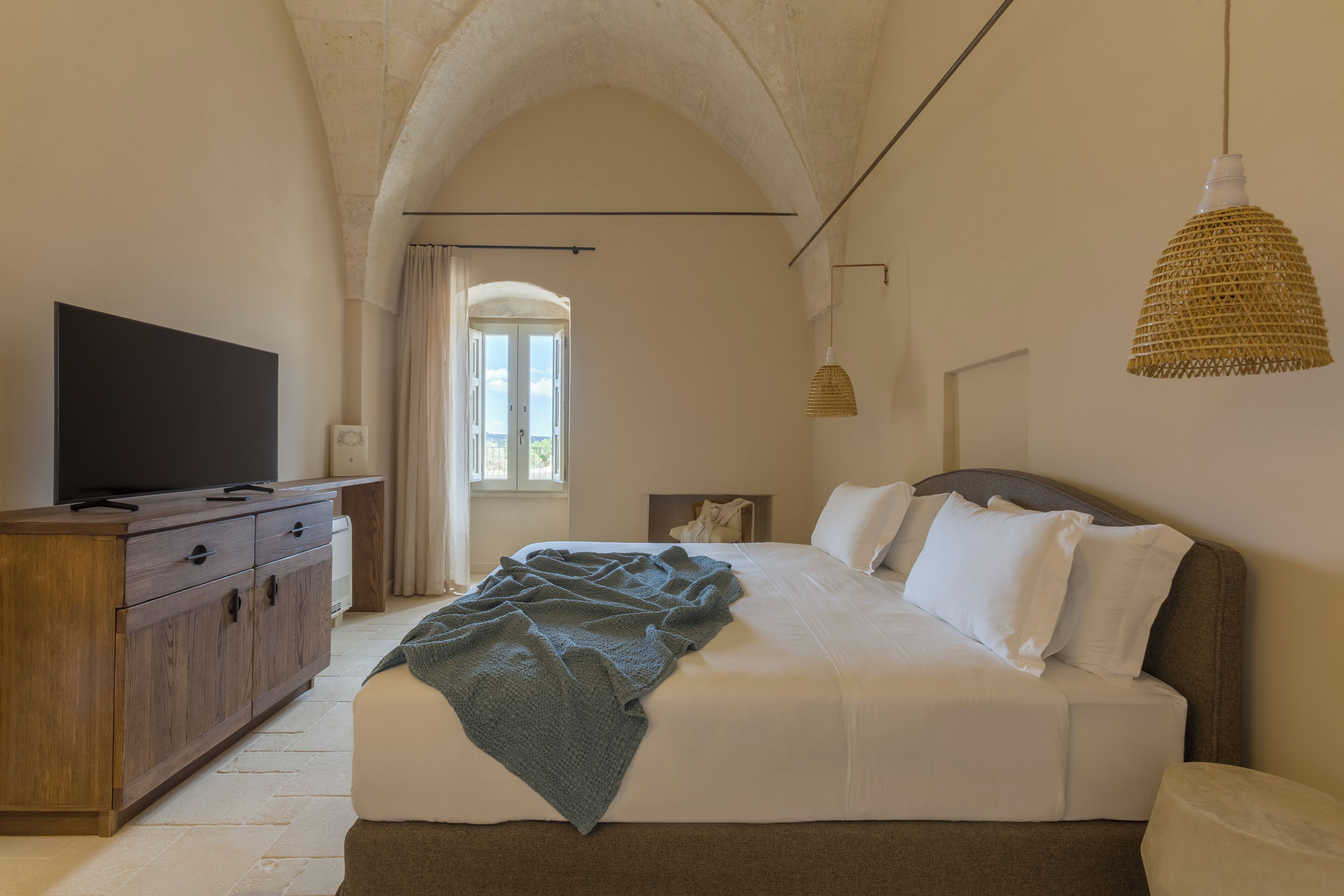 Un dormitorio con una cama grande, un aparador de madera, un televisor de pantalla plana y un ventanal con cortinas.