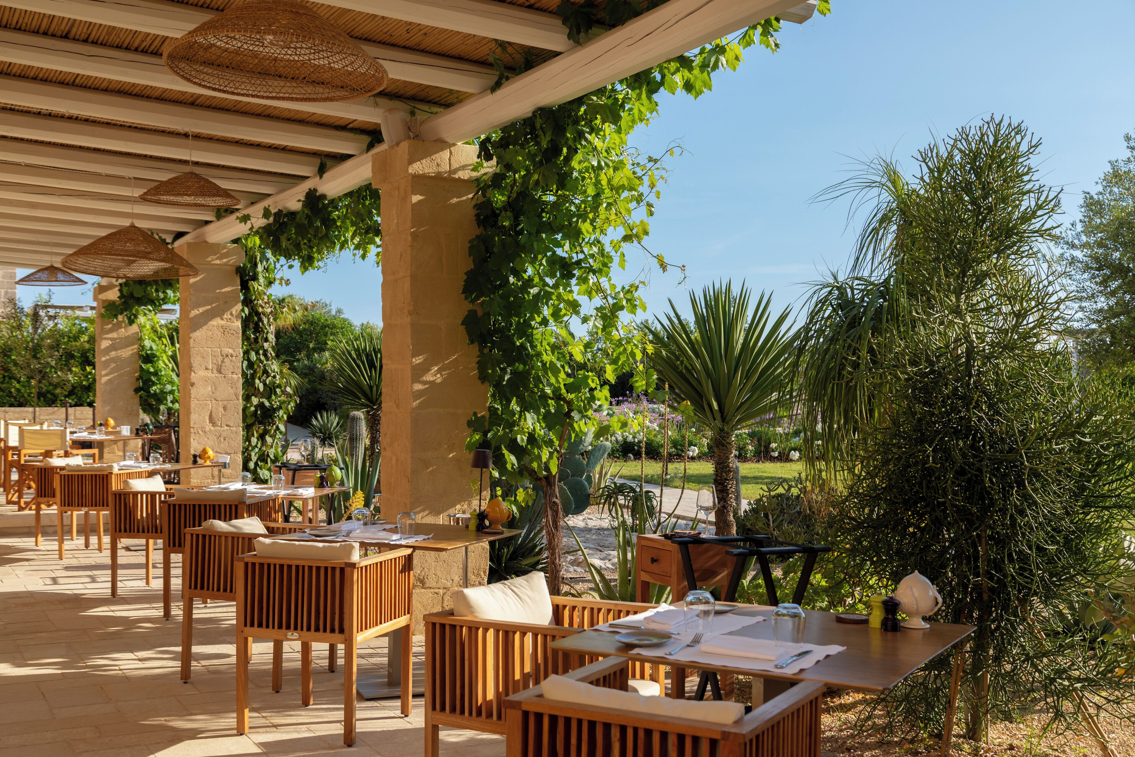 An outdoor patio with wooden furniture, a pergola, and greenery.