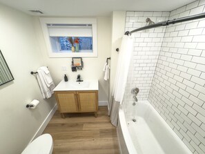 Une salle de bain avec un lavabo blanc, un meuble en bois, des toilettes et une baignoire avec un rideau de douche.