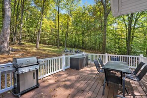 Une terrasse équipée d’un barbecue, d’un espace salon extérieur et offrant une vue sur une zone boisée.