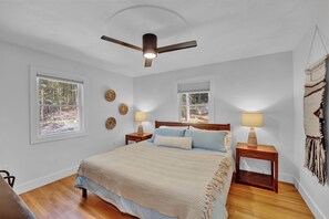Une chambre à coucher comprenant un lit, deux tables de chevet avec des lampes, un ventilateur de plafond et deux fenêtres.
