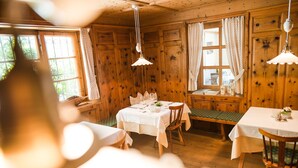 A wooden interior with a dining table set for two, a bench, and a window with curtains. - Hotel Kiendl (Schenna)