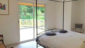 Ein Schlafzimmer mit einem Himmelbett, einem Sessel und Blick auf einen Balkon mit einem Geländer.
