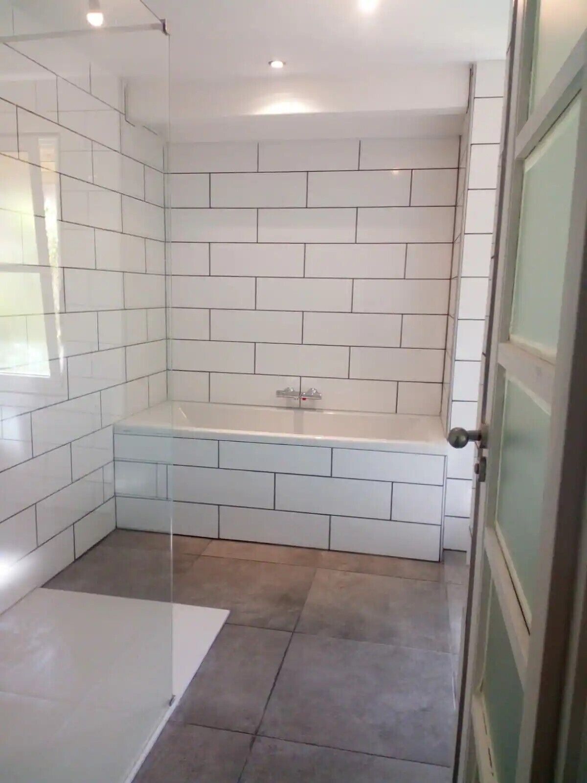 Un baño con paredes de azulejos blancos, cabina de ducha de vidrio y bañera.