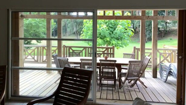 Ein überdachter Außenbereich mit Holzdeck, einem Tisch mit Stühlen und Blick auf einen Garten.
