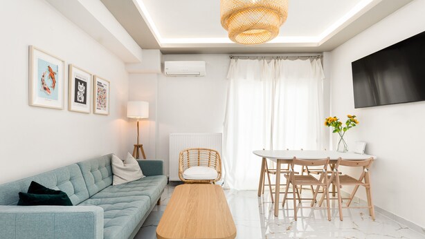 A modern living room with a sofa, a wooden bench, a dining table with chairs, and framed artwork on the wall. - Sunflower by halu! Apartments (Thessaloniki)
