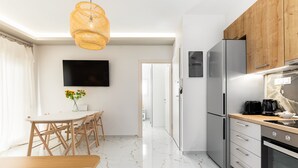 A modern kitchen with a dining area, a TV mounted on the wall, and a wooden ceiling light. - Sunflower by halu! Apartments (Thessaloniki)
