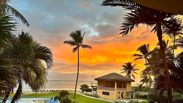 Un resort con piscina, palme e vista sull'oceano al tramonto.