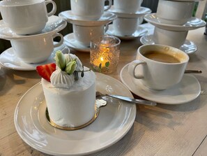 A dessert on a plate with a cup of coffee and multiple teacups in the background. - Marta 8 - House & Garden (Tallinn)