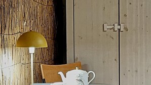 Una mesa de comedor con una tetera blanca, tazas, una lámpara amarilla y una silla de madera.