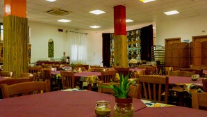 Um restaurante com várias mesas e cadeiras, um pilar central e uma parede estampada.