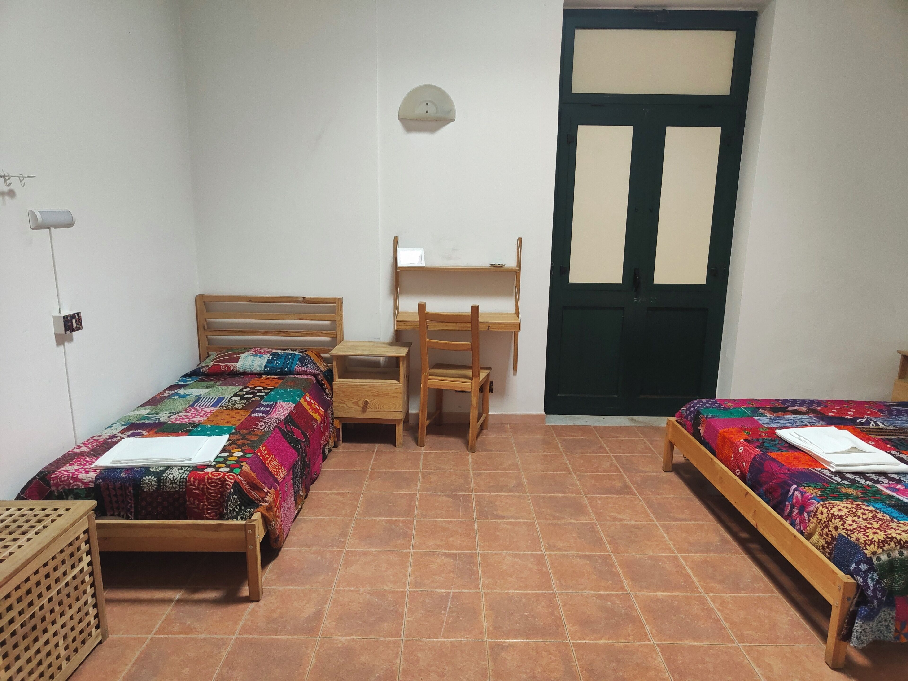 A dormitory room with two beds, a desk, and a chair.