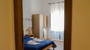 Quarto com cama, guarda-roupa, mesa de cabeceira e janela com cortinas.