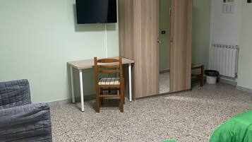 Una habitación con cama, una silla, un escritorio, un armario, un televisor y un radiador.