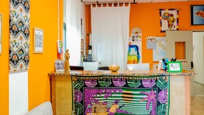 Uma área de recepção com um balcão colorido, uma cortina branca e várias decorações, incluindo um mapa e quadros.