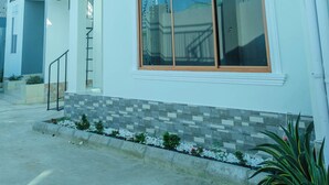 Un edificio de dos pisos con balcón, ventanas amplias y un pequeño jardín.