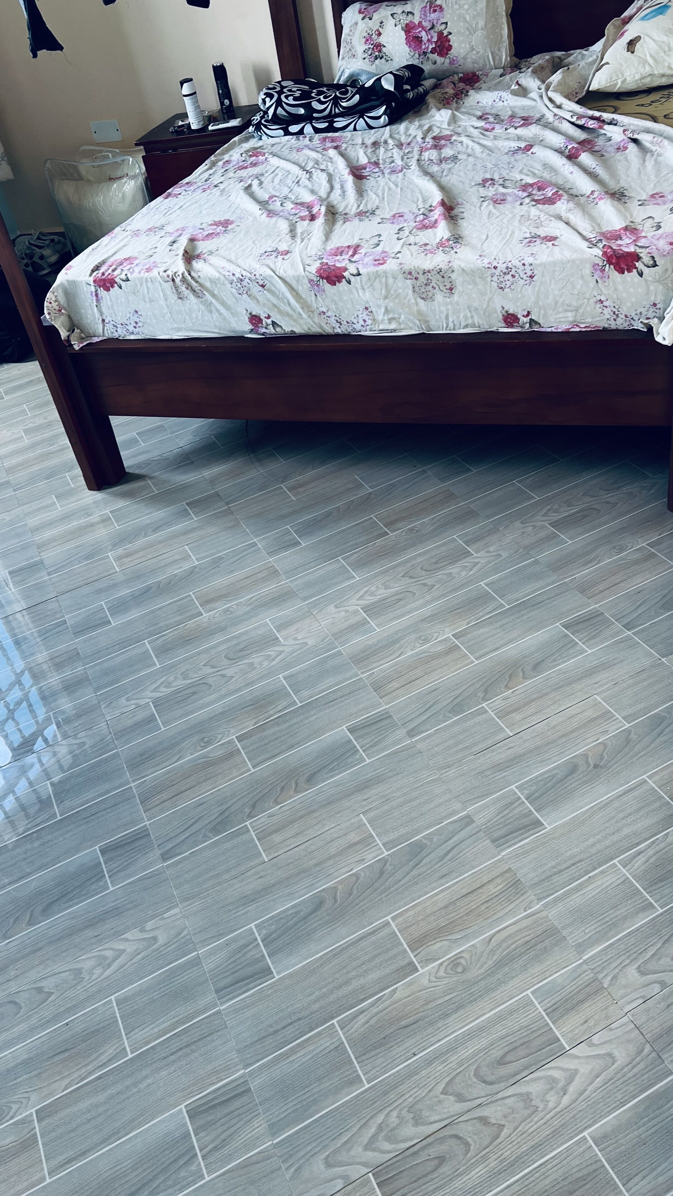A bed with a floral bedspread, a wooden headboard, and a grey patterned floor.