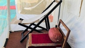 Um quarto com tenda, uma cama, uma cadeira e uma pequena mesa.