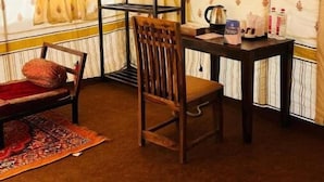Um quarto aconchegante com cortina estampada, uma cadeira de madeira, uma mesa pequena com uma chaleira e uma janela com cortinas.