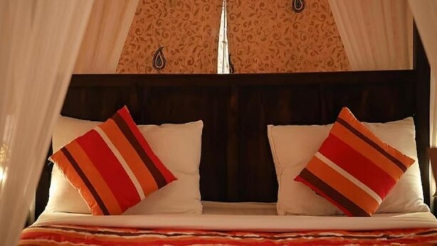 Cama com duas almofadas, manta listrada e dossel.