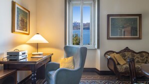Une pièce avec vue sur un lac, un fauteuil bleu, une table en bois avec des appareils électroniques, un canapé et des carreaux de sol à motifs.
