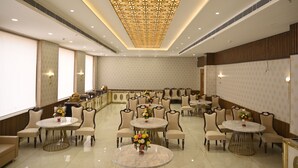 A spacious banquet hall with round tables and chairs, a decorative ceiling, and wall-mounted lighting. - The Velvista Hotel (Muzaffarnagar)