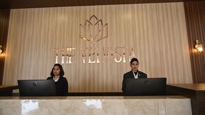 A reception desk with two individuals seated behind it, a wooden wall with the text "THE NEVISTA" and a logo above. - The Velvista Hotel (Muzaffarnagar)