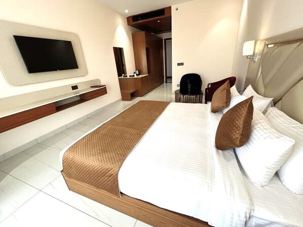 Una habitación de hotel moderna con una cama grande, un televisor de pantalla plana montado en la pared, un cabecero de madera y un rincón de descanso con una silla y una mesita.