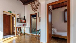 A hallway with a wooden door, a small table with a vase, a chair, and a bed in the adjacent room. - Solemar Sicilia - Casa Ernesto  (Santa Flavia)